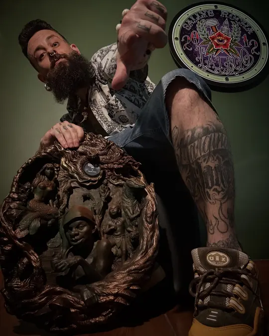 Sallys Rocha no estúdio, ao lado do troféu do Master Ink, uma escultura em bronze, com o selo da Sallys Rocha Tattoo na parede verde.